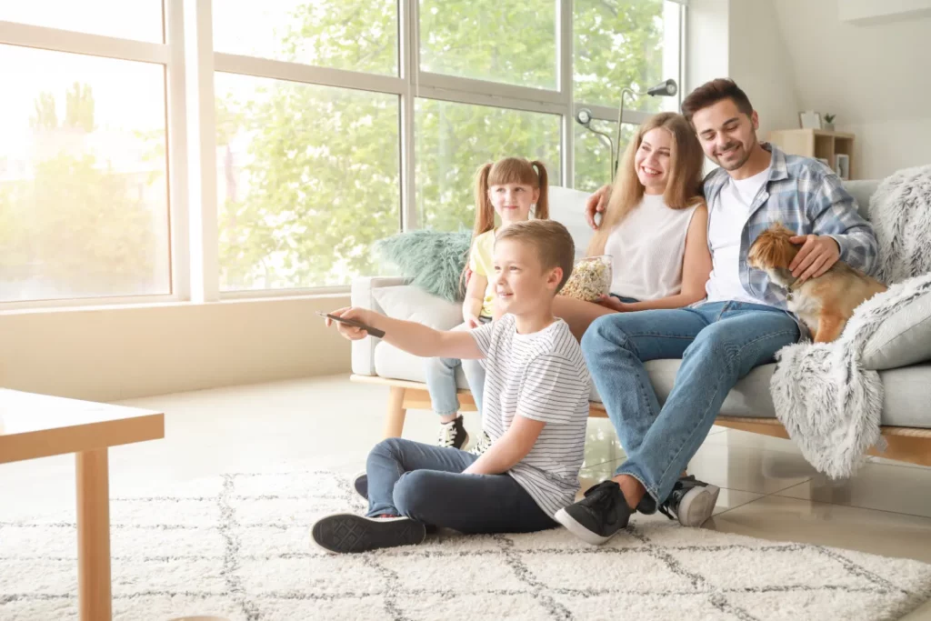 A family of four sitting on a white couch in a well-lit living room.